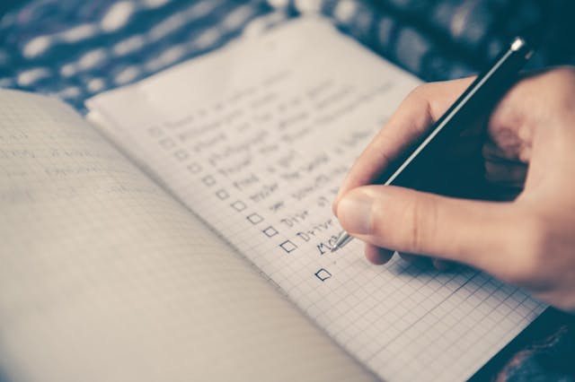 An open notebook with a checklist. A hand holds a pen and is about to check off the bottom checkbox.